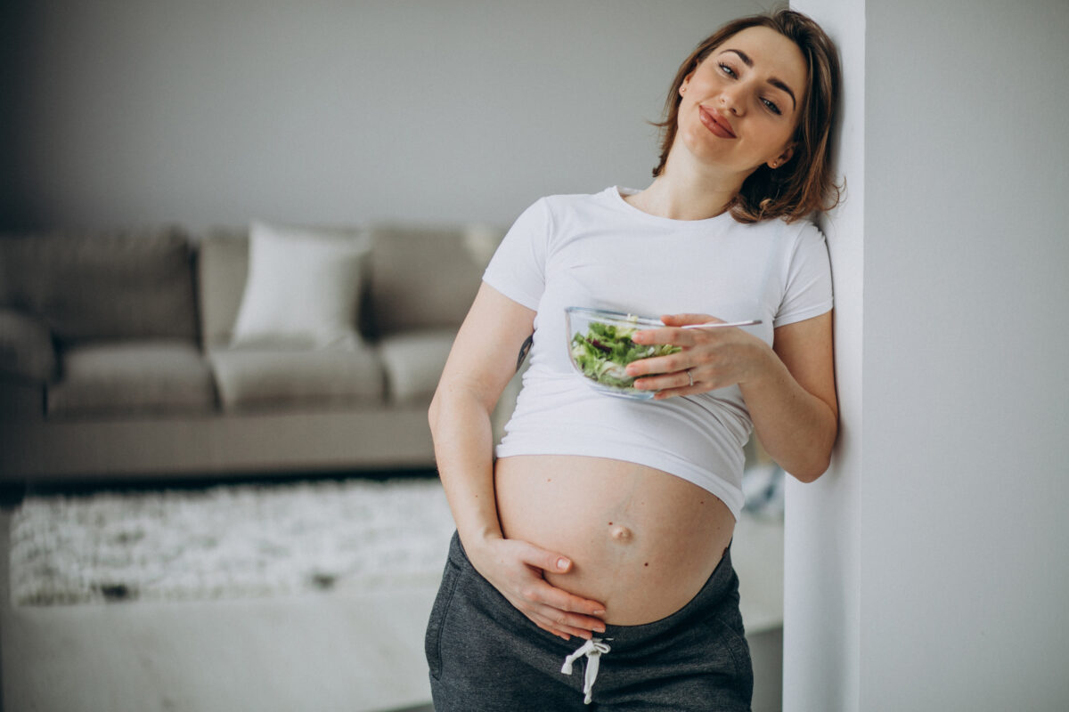 Young pregnant woman eating salad at home